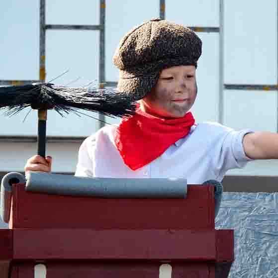 A young boy wearing a hat and scarf is holding a chimney brush.