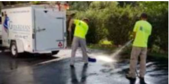 Two men are cleaning a driveway with a trailer in the background.