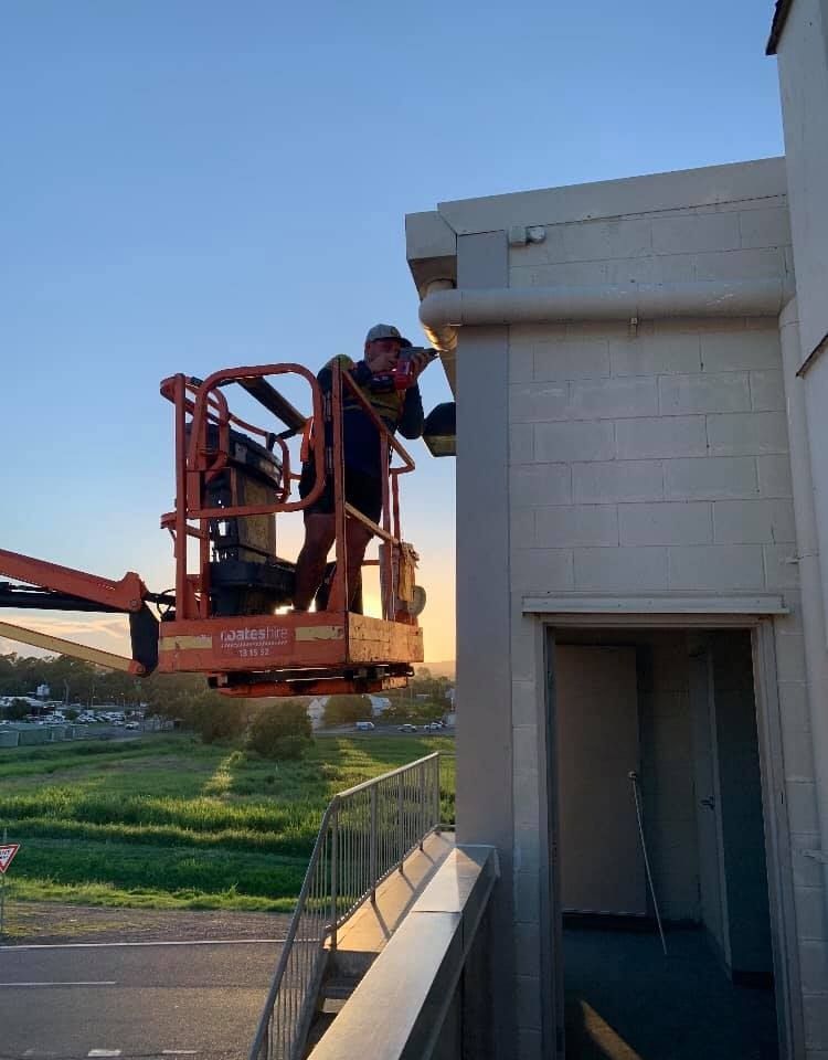 A Man is Working on the Side of a Building on a Lift — Reed Plumbing Industries in Mackay, QLD