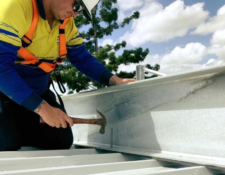 A Man is Working on a Roof With a Hammer — Reed Plumbing Industries in Mackay, QLD