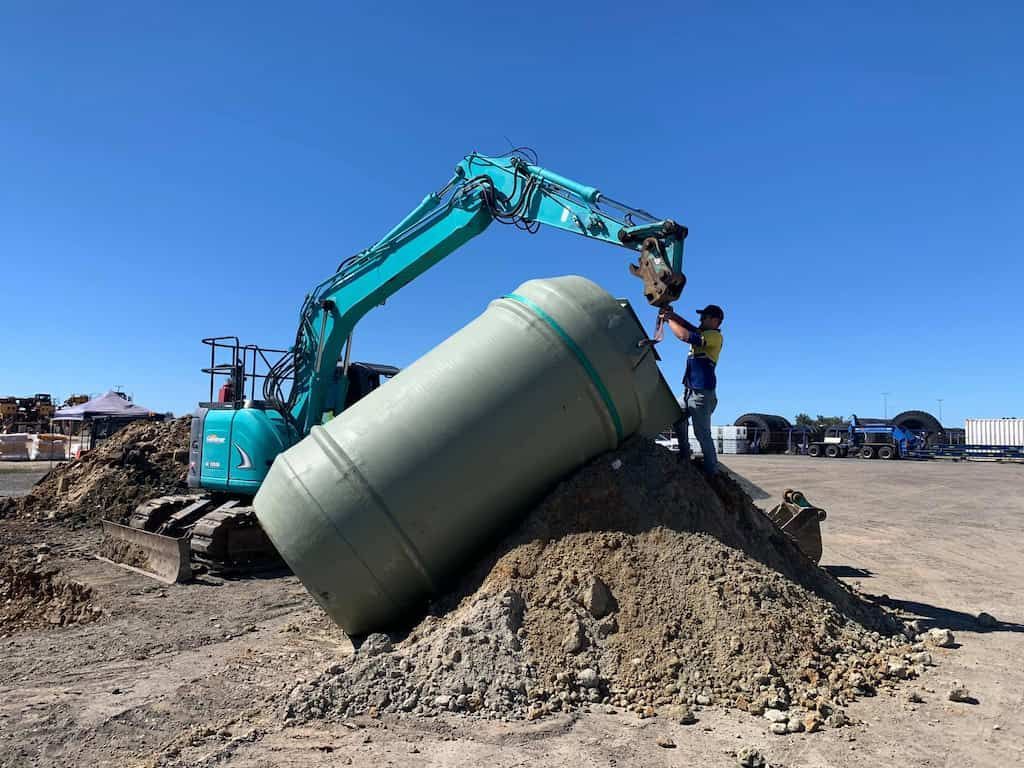 A Man is Standing on Top of a Pile of Dirt Next to an Excavator — Reed Plumbing Industries in Mackay, QLD
