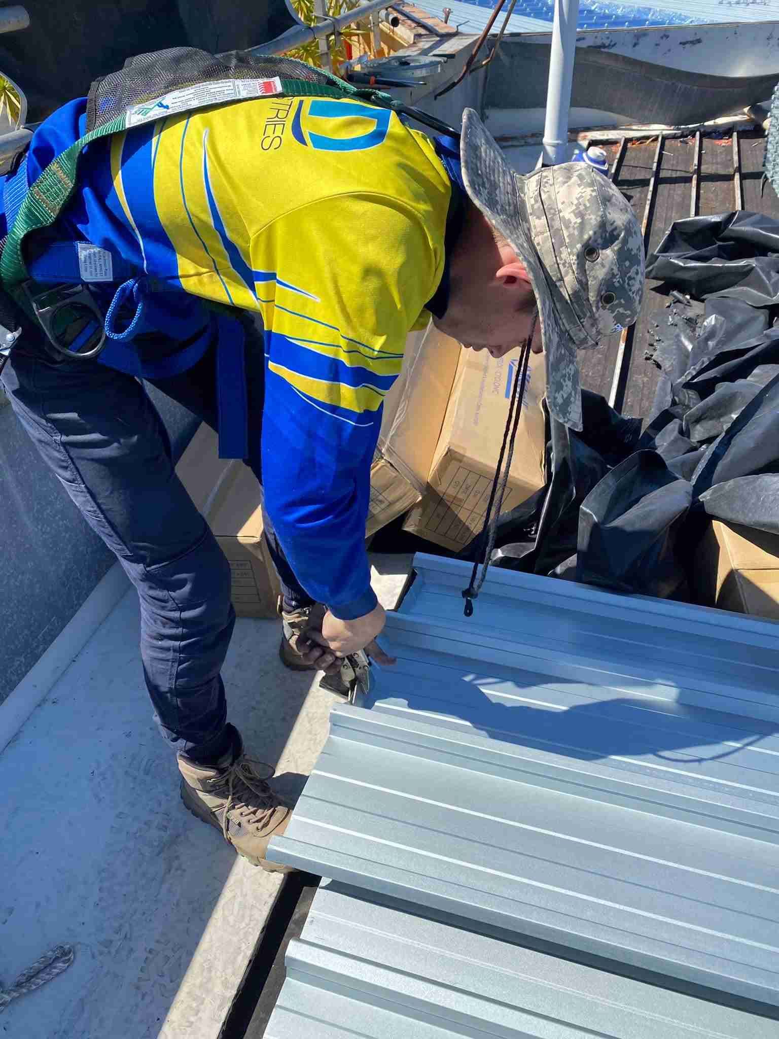 A Man in a Blue and Yellow Shirt is Working on a Metal Roof — Reed Plumbing Industries in Mackay, QLD