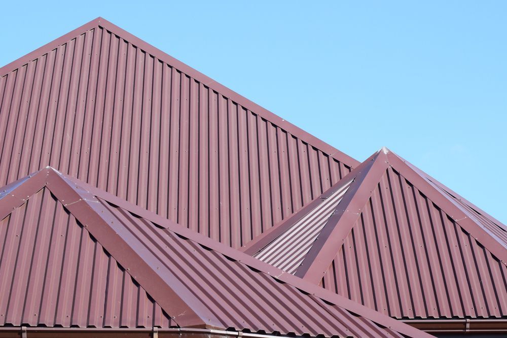 Red Metal Rooftops with Triangular Peaks Against a Blue Sky — Reed Plumbing Industries in Mackay, QLD