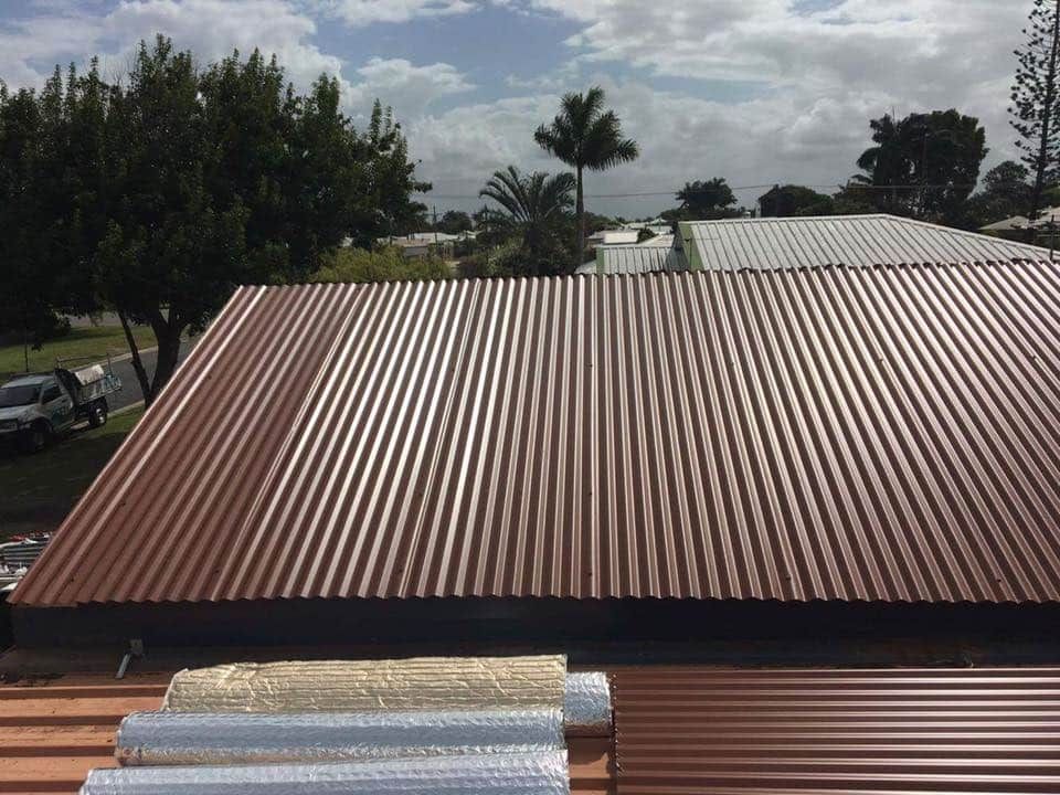A Brown Corrugated Metal Roof With Trees in the Background — Reed Plumbing Industries in Mackay, QLD