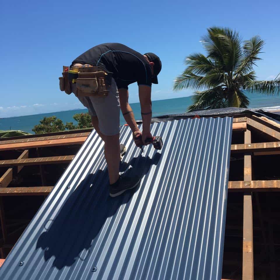 A Man is Working on a Roof With the Ocean in the Background — Reed Plumbing Industries in Mackay, QLD