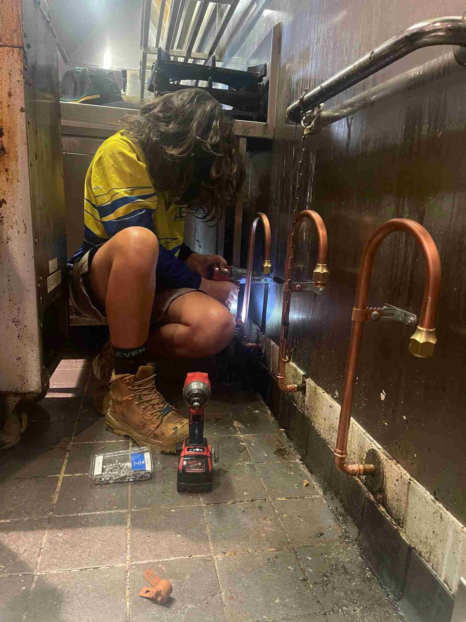 A Man is Welding Pipes in a Kitchen With a Drill — Reed Plumbing Industries in Mackay, QLD