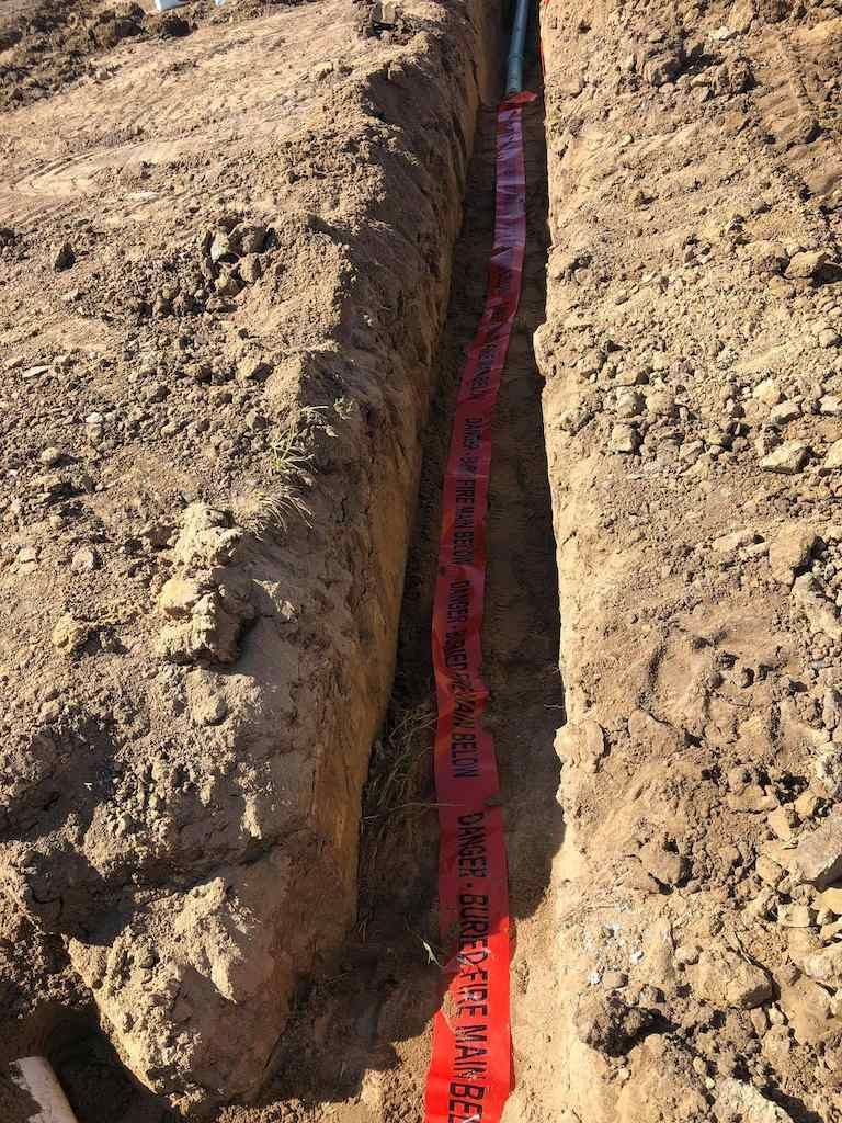 A Red Caution Tape is Laying in the Dirt Next to a Pipe — Reed Plumbing Industries in Mackay, QLD