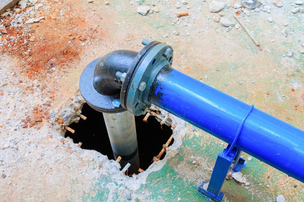 A Blue Pipe is Coming Out of a Hole in the Ground — Reed Plumbing Industries in Gladstone, QLD