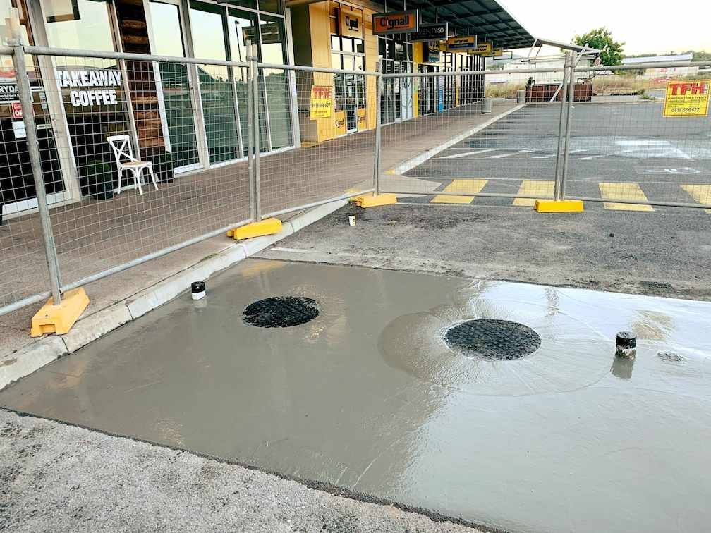 A Manhole Cover is Being Installed on the Sidewalk in Front of a Building — Reed Plumbing Industries in Mackay, QLD