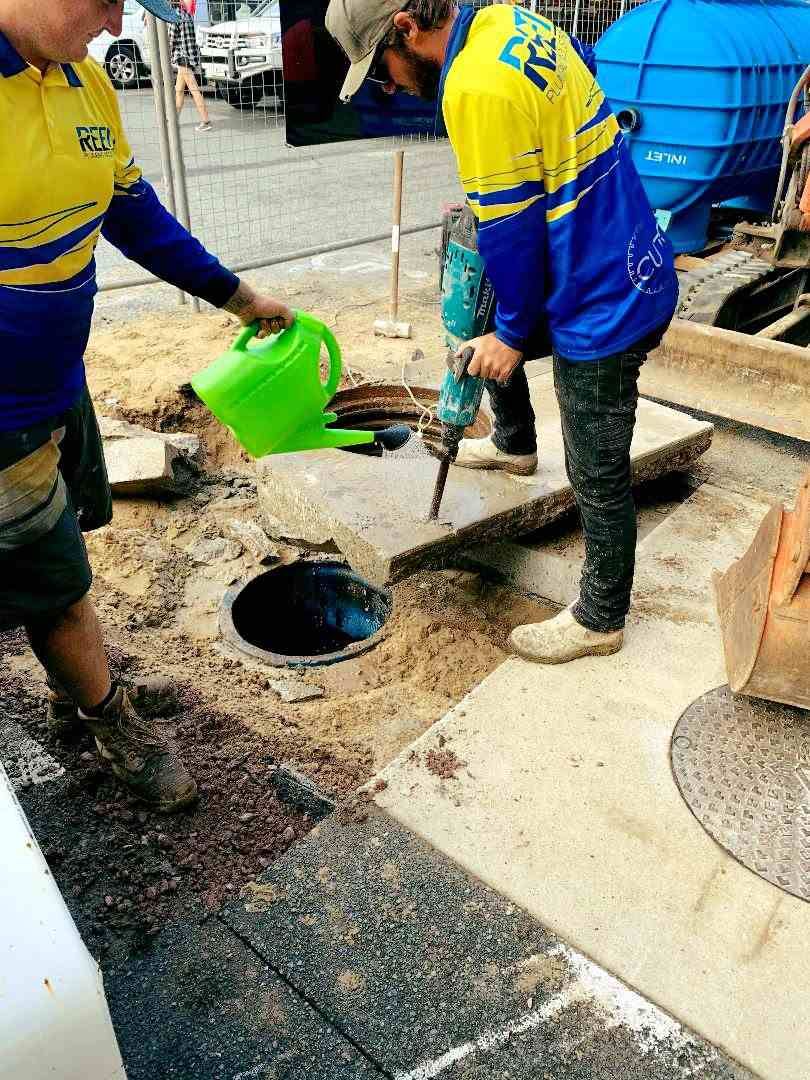 A Man is Pouring Water From a Green Can Into a Manhole — Reed Plumbing Industries in Mackay, QLD