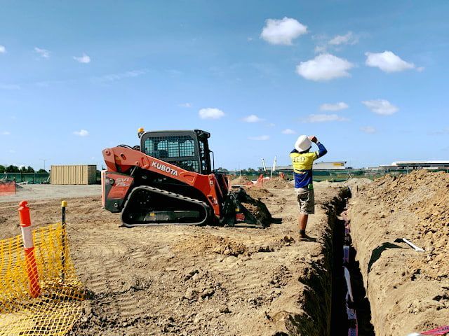 A Man is Standing in a Trench Next to a Bulldozer — Reed Plumbing Industries in Mackay, QLD