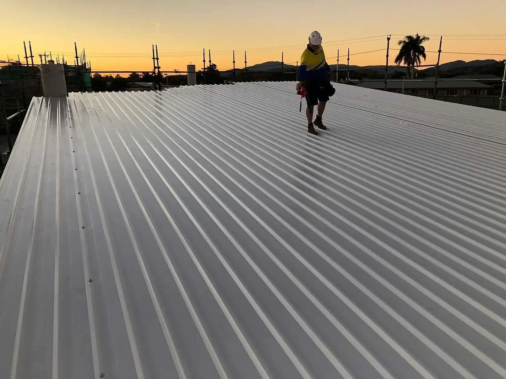 A Man is Standing on Top of a White Roof — Reed Plumbing Industries in Mackay, QLD