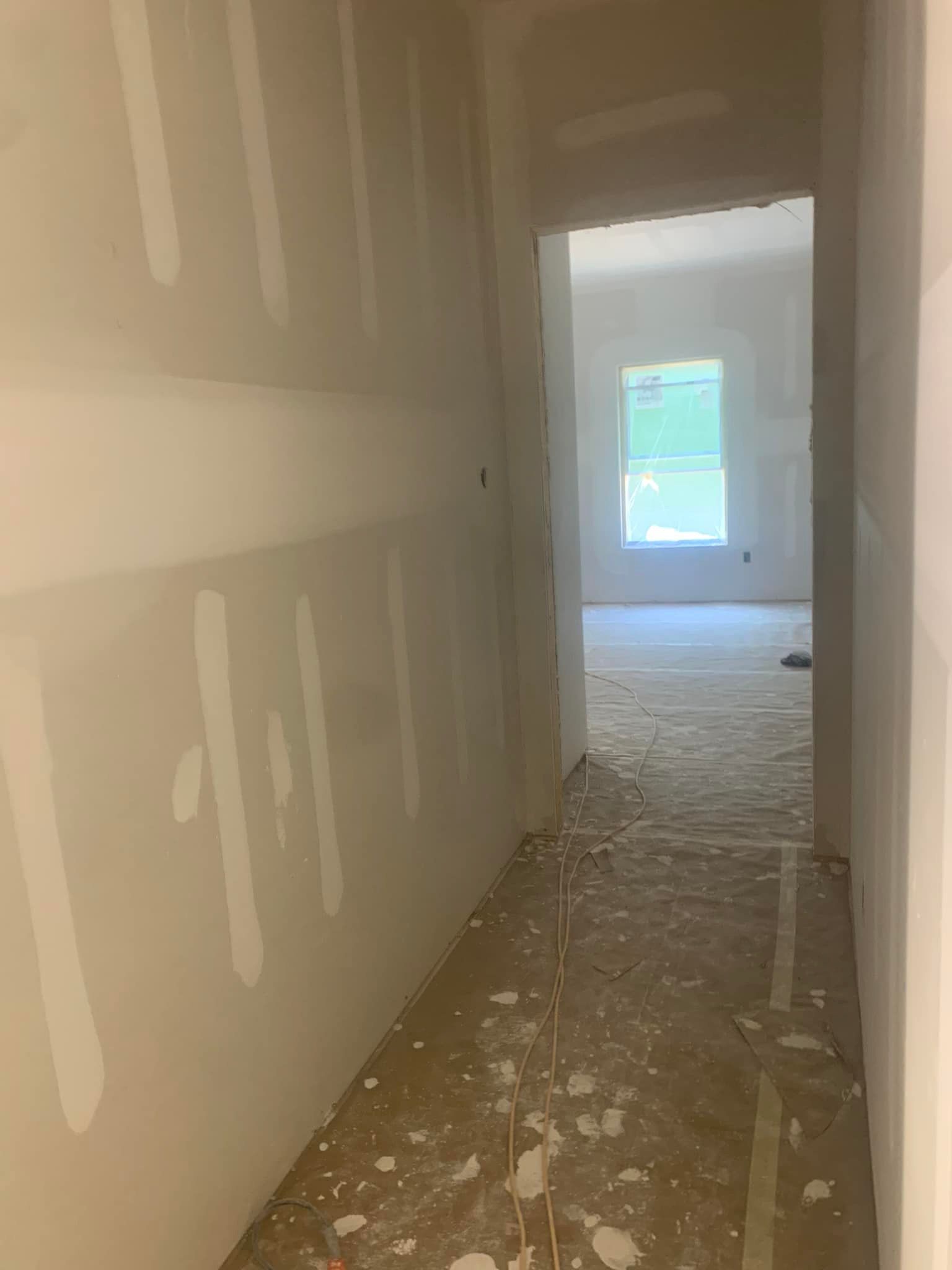 Hallway under construction, drywall installed, leading to a room with a window.
