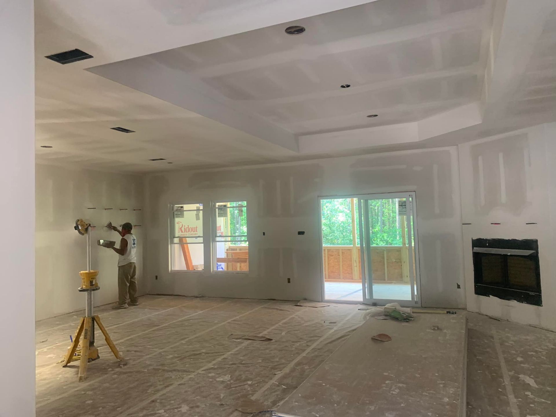 Person working on drywall in a room with a sliding glass door and a fireplace.