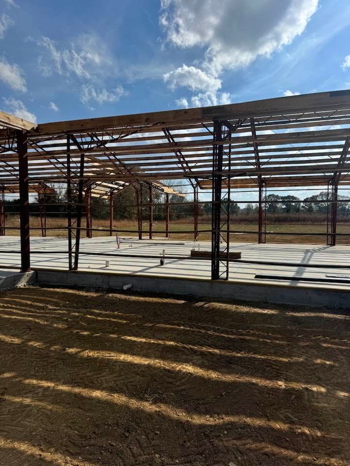 Steel frame construction of a large building under a blue sky. Concrete foundation with exposed beams and supports.