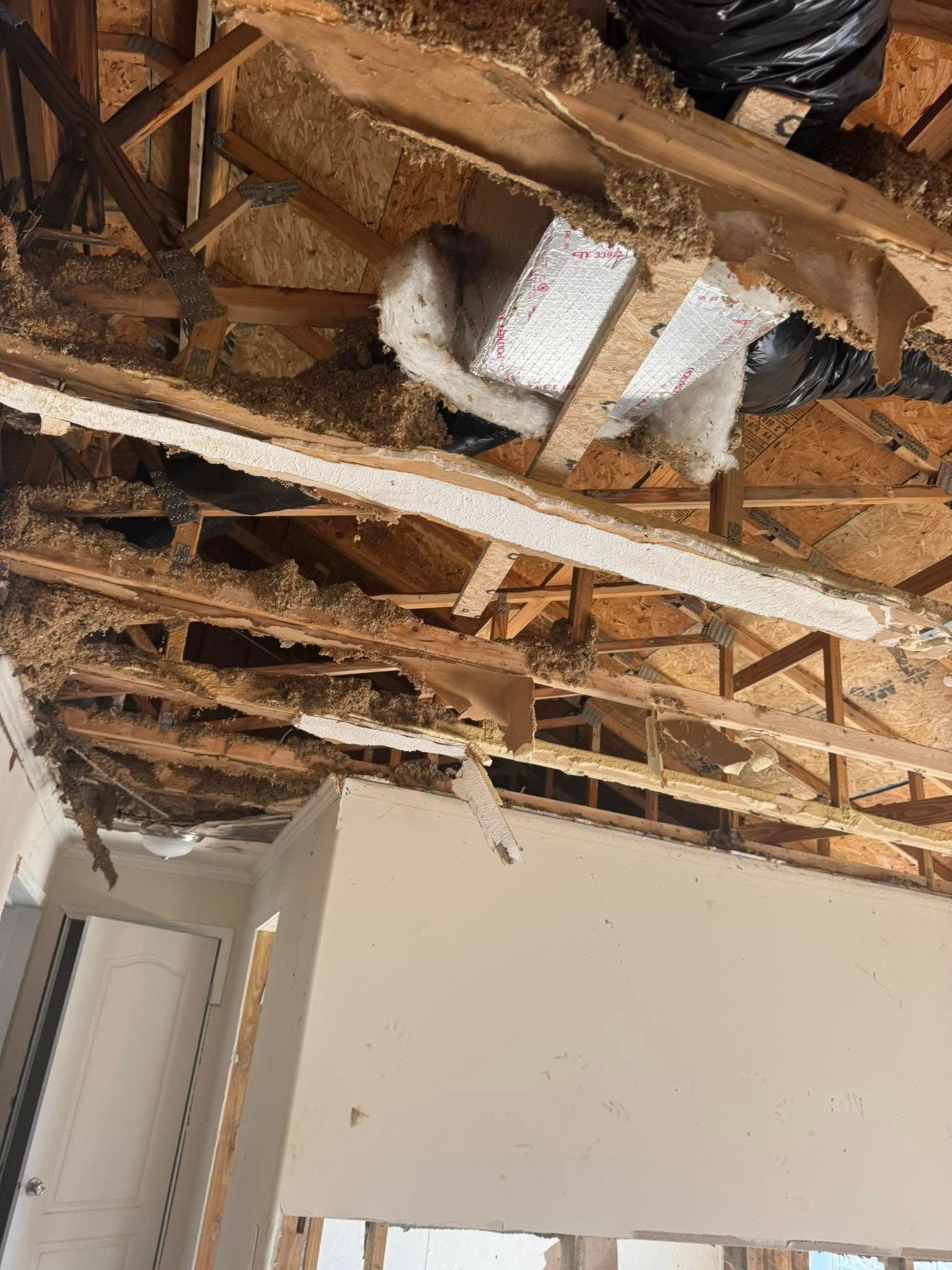 Damaged ceiling showing exposed wooden beams and insulation. Debris scattered throughout.