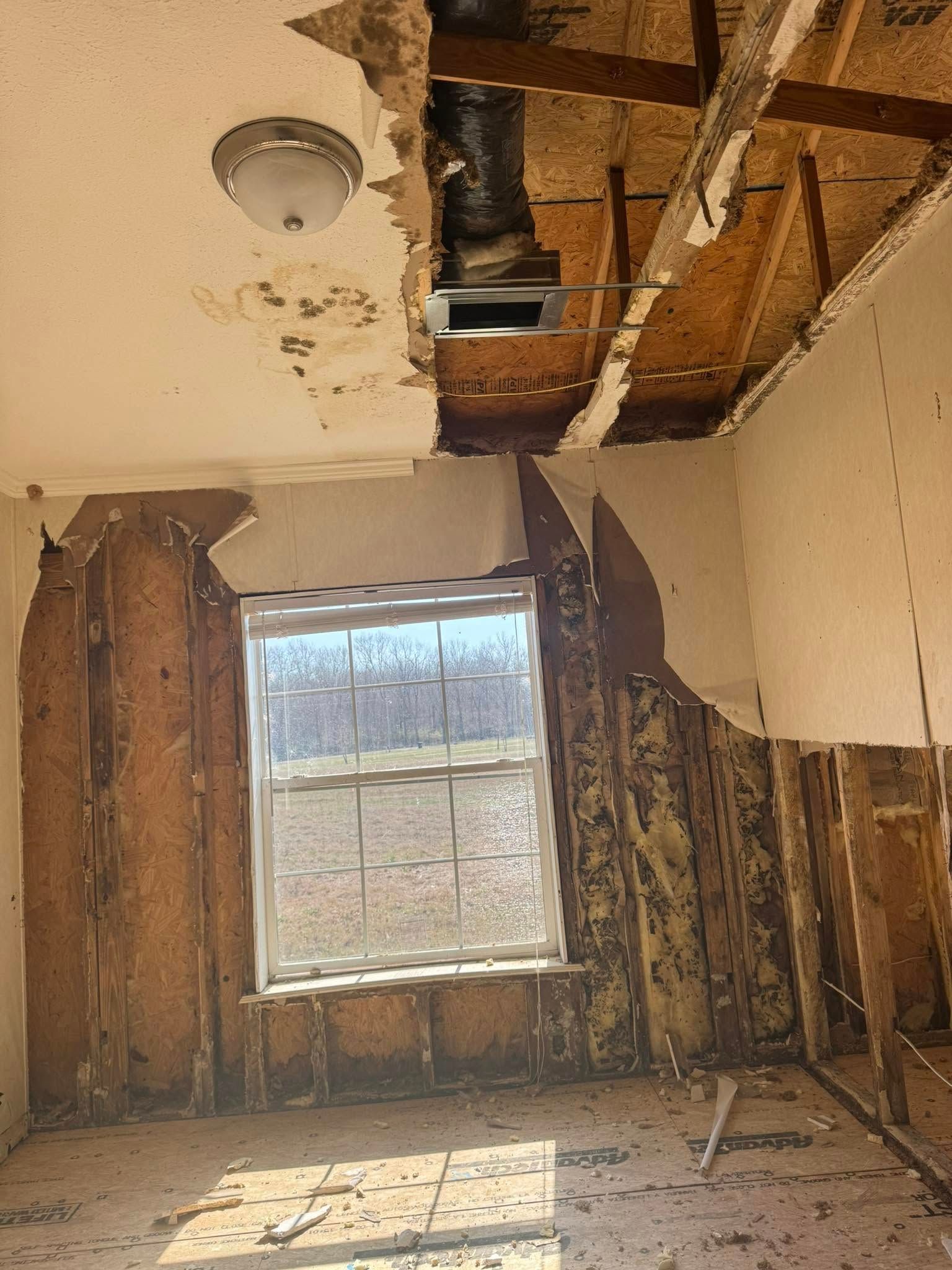 Damaged interior room with exposed ceiling and walls, window, and debris.