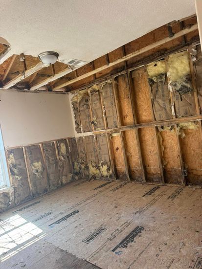 Room gutted to the studs; exposed beams, insulation, and plywood flooring.