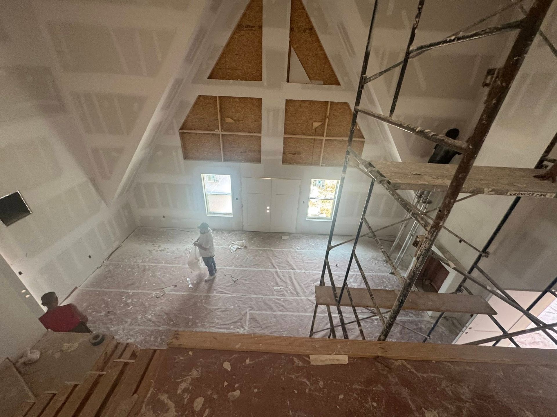 Construction in progress: Interior view of a high-ceilinged room with scaffolding, drywall, and workers.