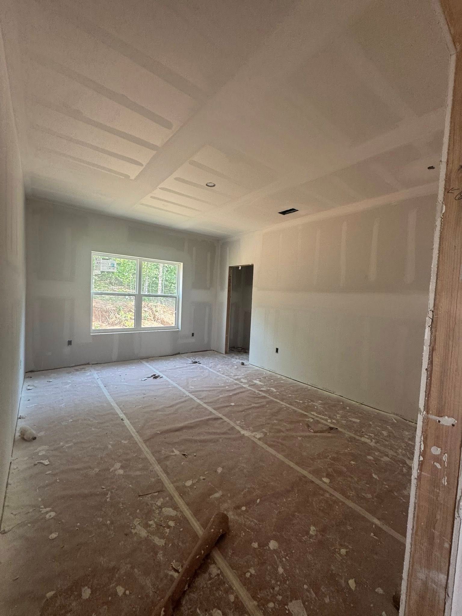 Interior of a room under construction; drywall walls, window, doorway, debris on the floor, unfinished.