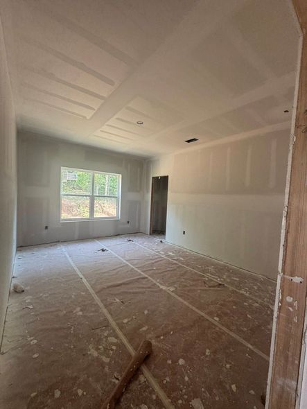Interior of a room under construction; drywall walls, window, doorway, debris on the floor, unfinished.