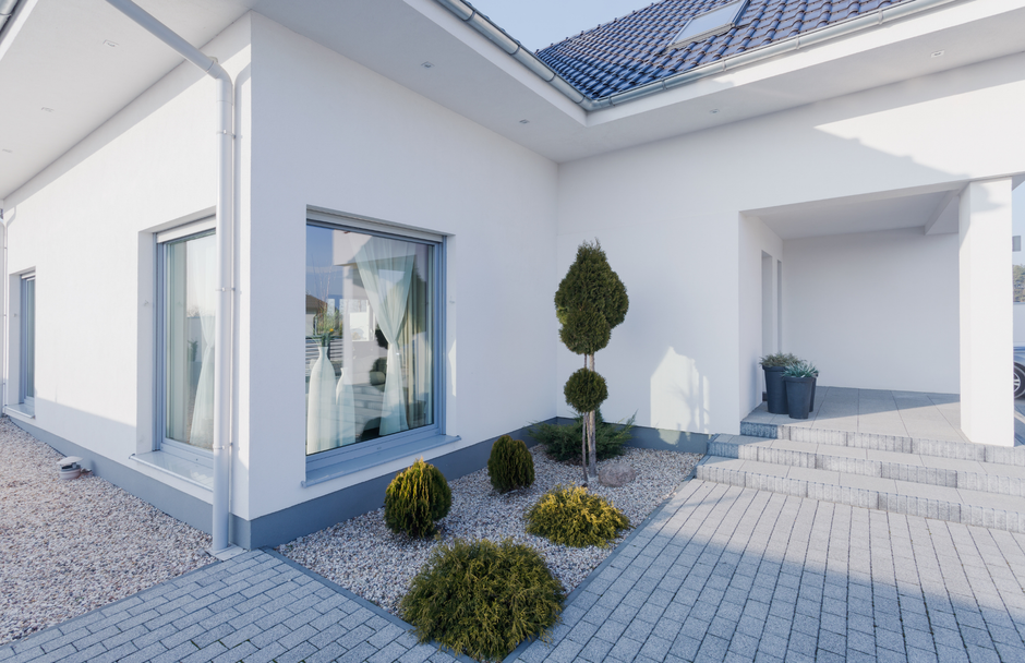 Modern white house with gray accents, small trees, and a brick pathway.