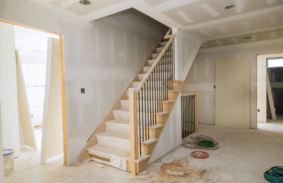 Interior view of a house under construction. Stairs with black spindles lead up to a second level.