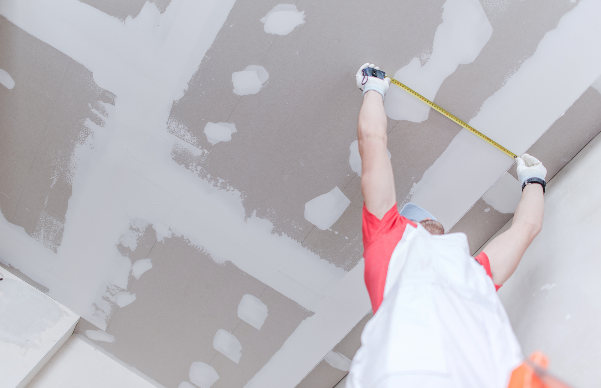 Construction worker measures ceiling with a tape measure.