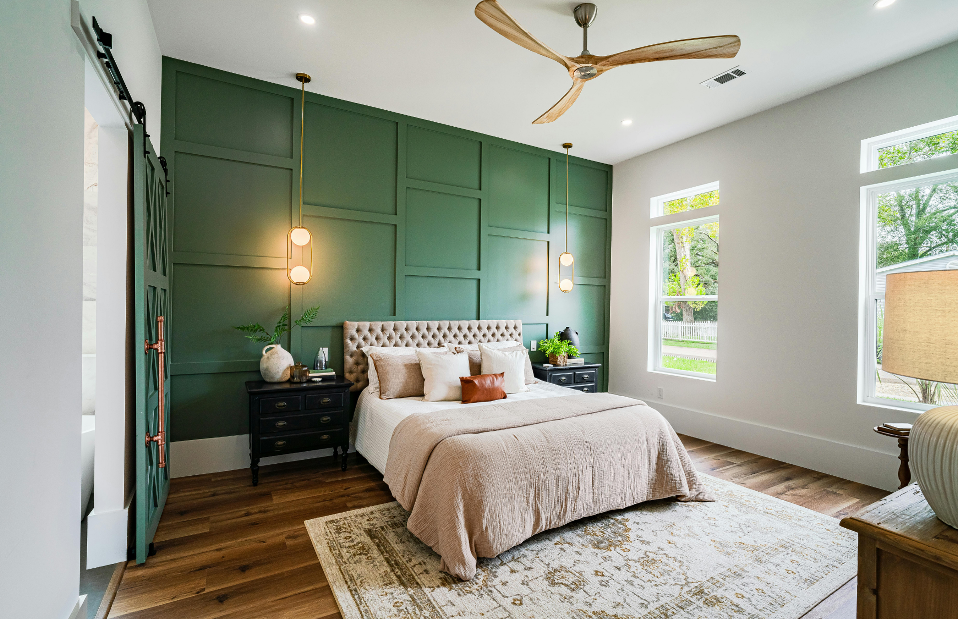 Bedroom with green accent wall, bed, wood floor, rug, and open sliding barn door.