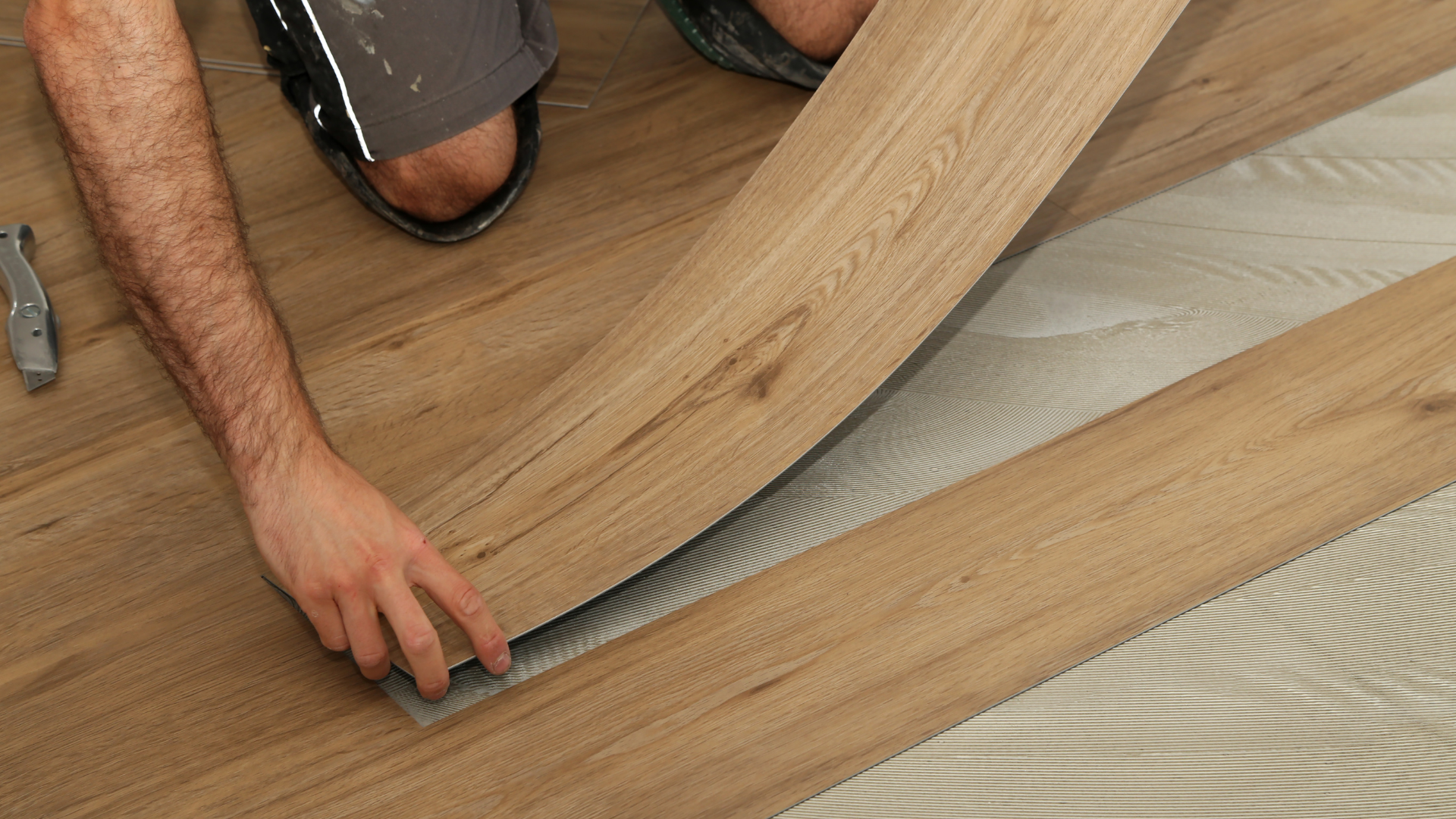 Person installing vinyl plank flooring; beige wood-look planks with curved flexible piece being laid.