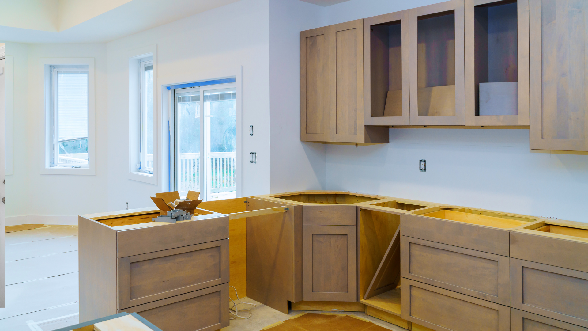 Kitchen under construction, unfinished cabinets in light wood, open space, and windows.
