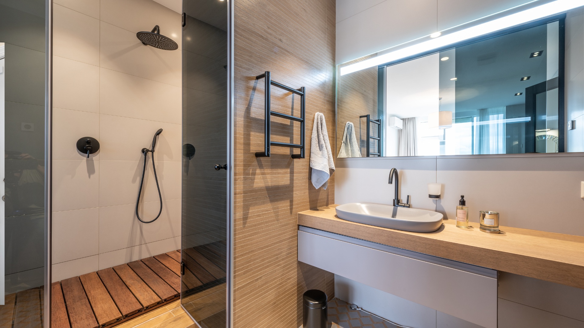 Modern bathroom with a shower, sink, and mirror. Black fixtures, wooden floor.