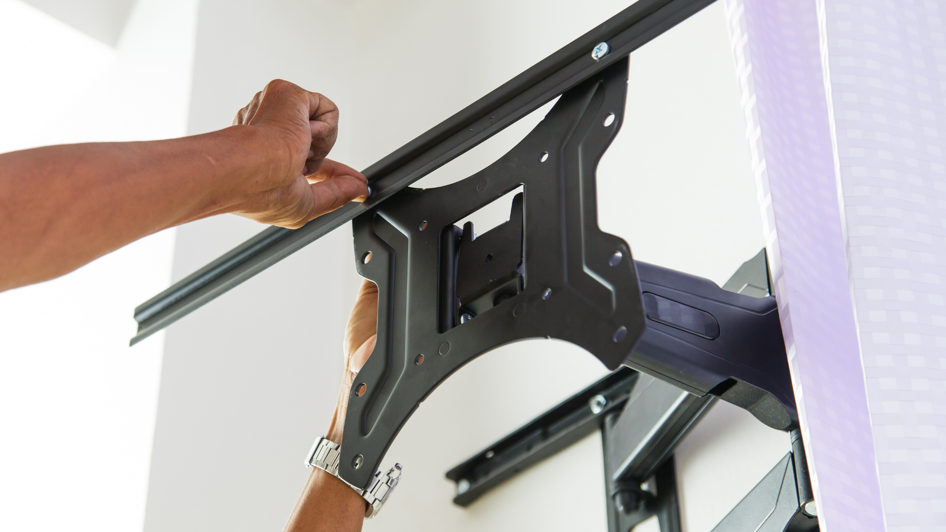 Person mounting a black TV bracket on a white wall, holding a track.