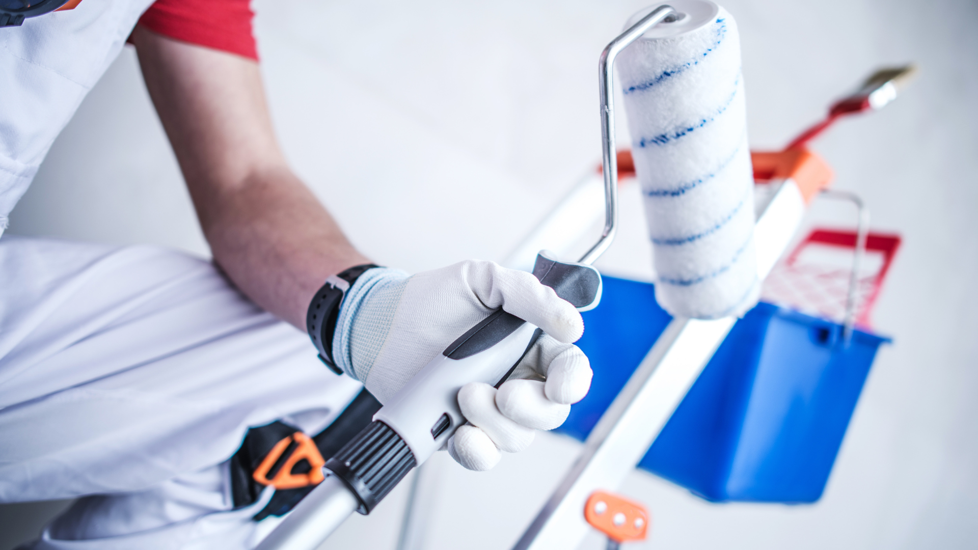 Painter on a ladder holding a paint roller, wearing white gloves and clothing. Blue bucket in the background.