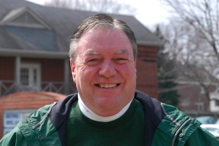 A man in a green jacket is smiling in front of a house