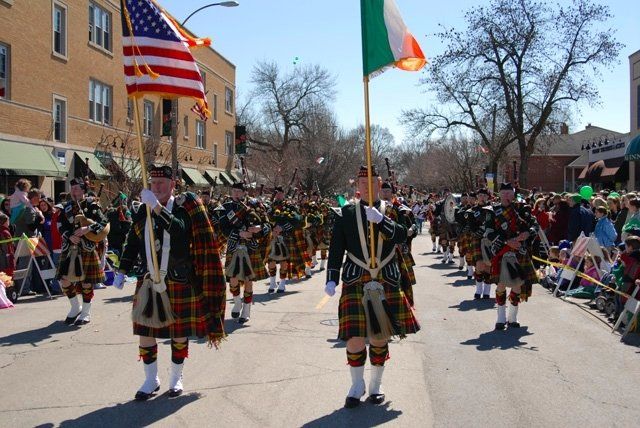 A group of men in kilts march down a street holding flags