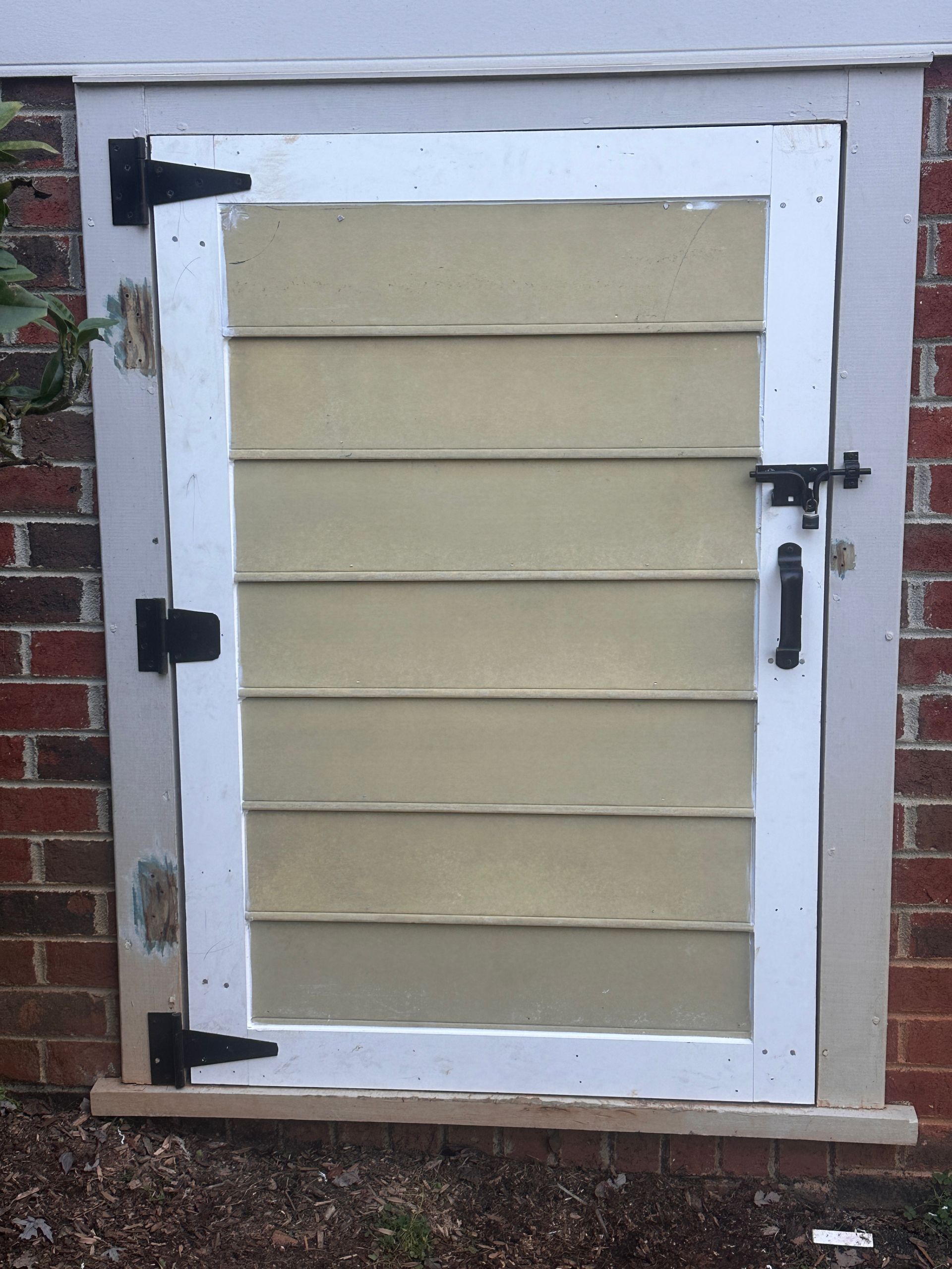Tan and white wooden door on a brick wall, with black hinges, latch, and handle.