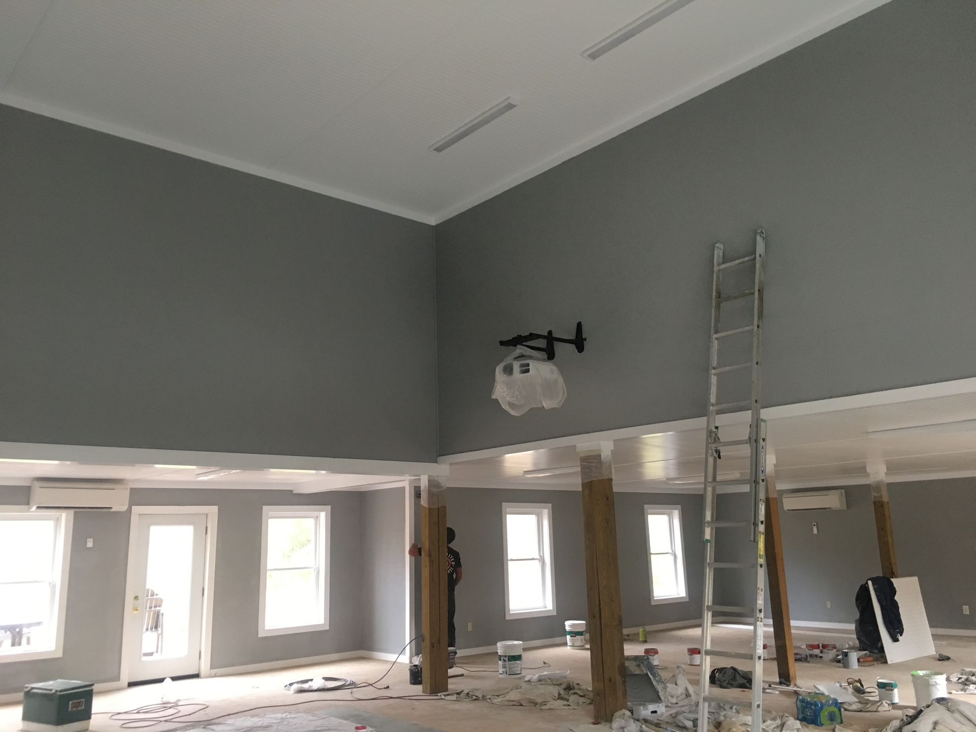 Interior of a room under renovation; gray walls, white ceiling and trim, ladder, projector, and exposed support beams.