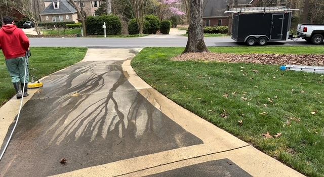 Person pressure washing a concrete driveway; streaks of water create a pattern.