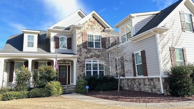 Two-story house with stone and beige siding, brown shutters, and a blue sky.