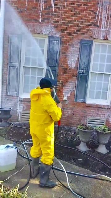 Person in yellow suit power washing a brick building.
