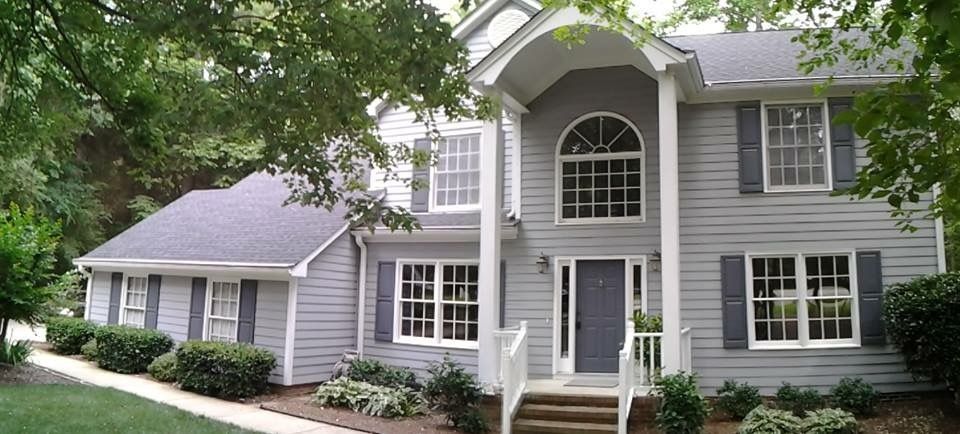 Two-story gray house with white trim, shutters, and arched front window. Trees surround.