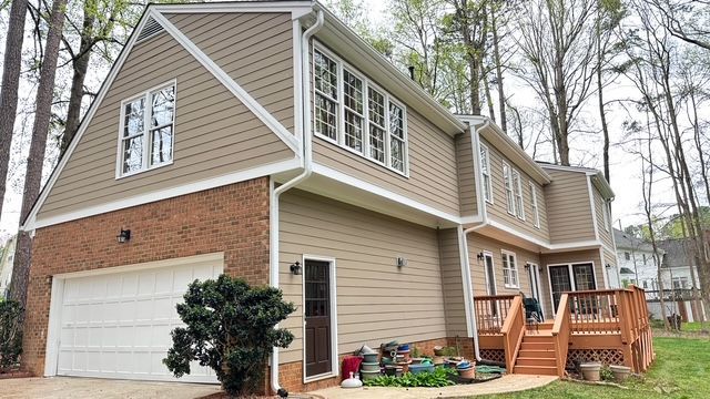 Two-story house with a brick garage, tan siding, and a wooden deck.