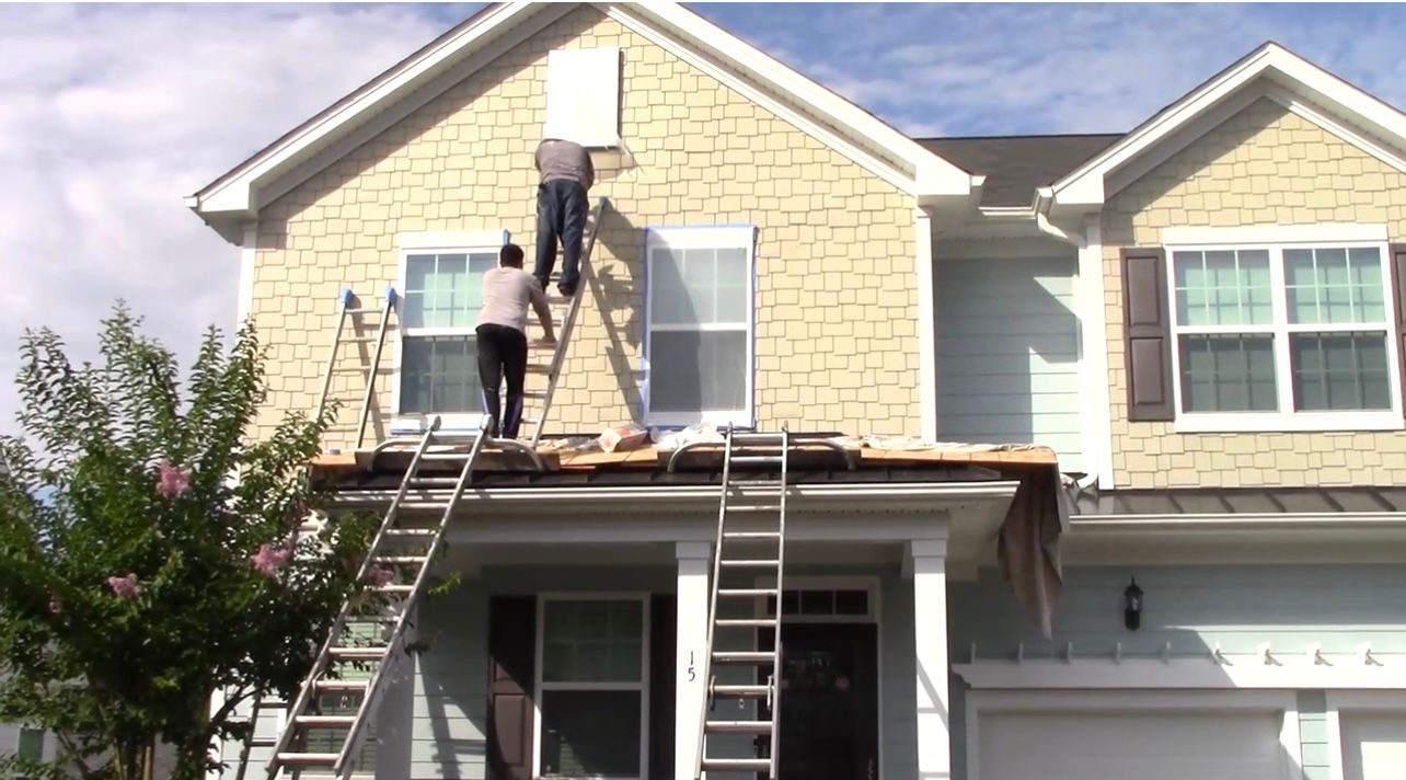 Two people on ladders working on the siding of a two-story house.