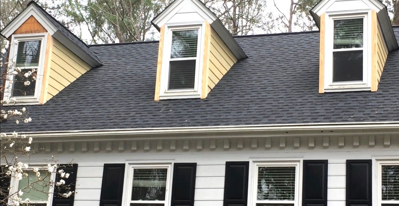 A house with a black roof, three dormer windows, and black shutters on a white facade.