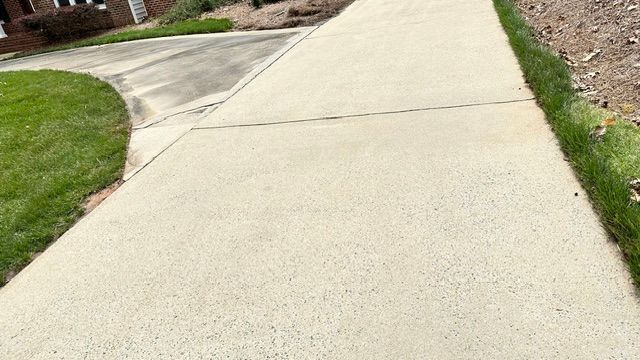 Concrete sidewalk next to grass. The sidewalk curves near the driveway and house.