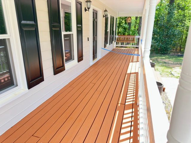 Long wooden porch painted with brown stain. White house with black shutters.
