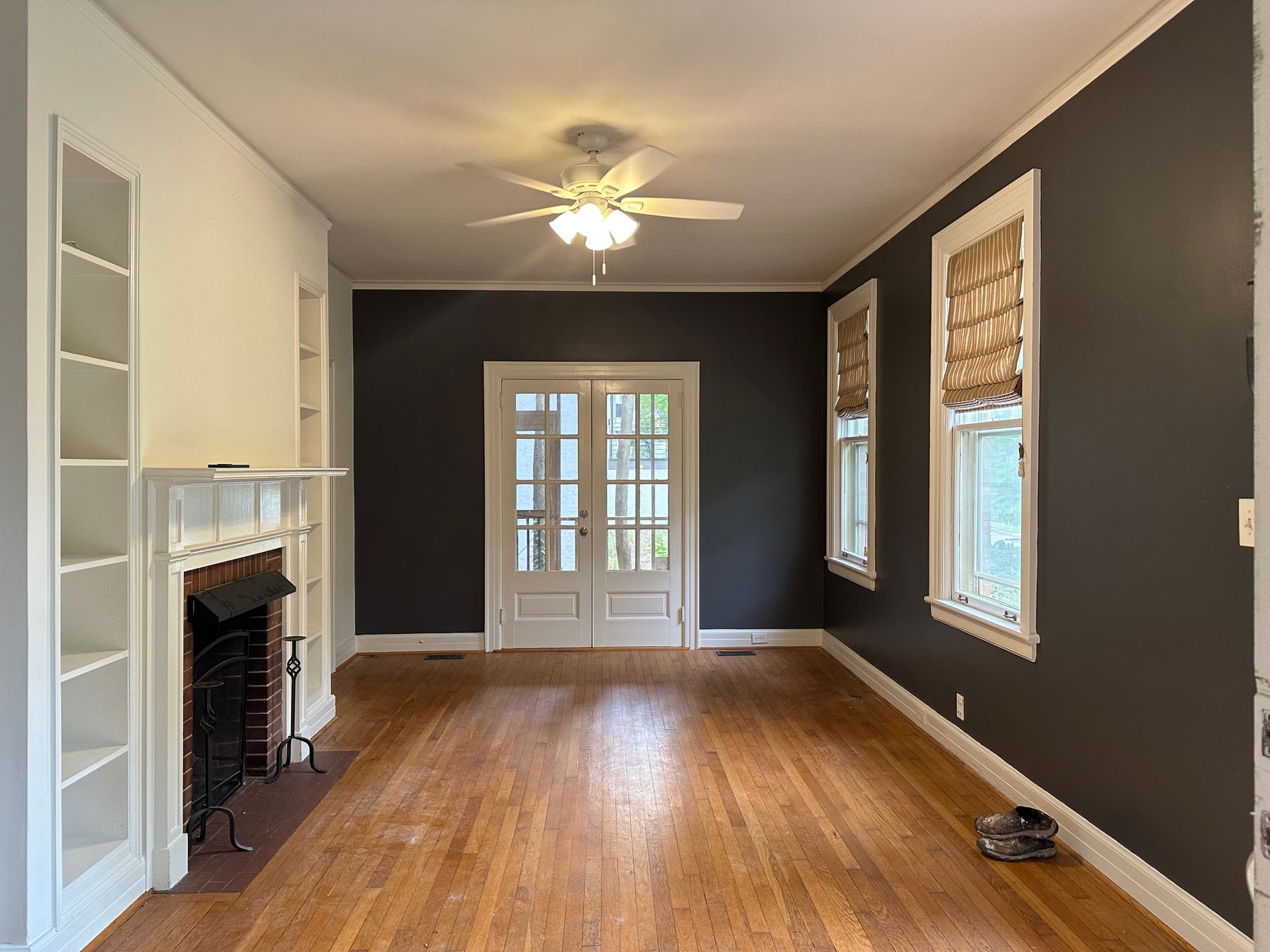 Empty living room with dark gray walls, hardwood floors, fireplace, built-in shelves, and double doors.