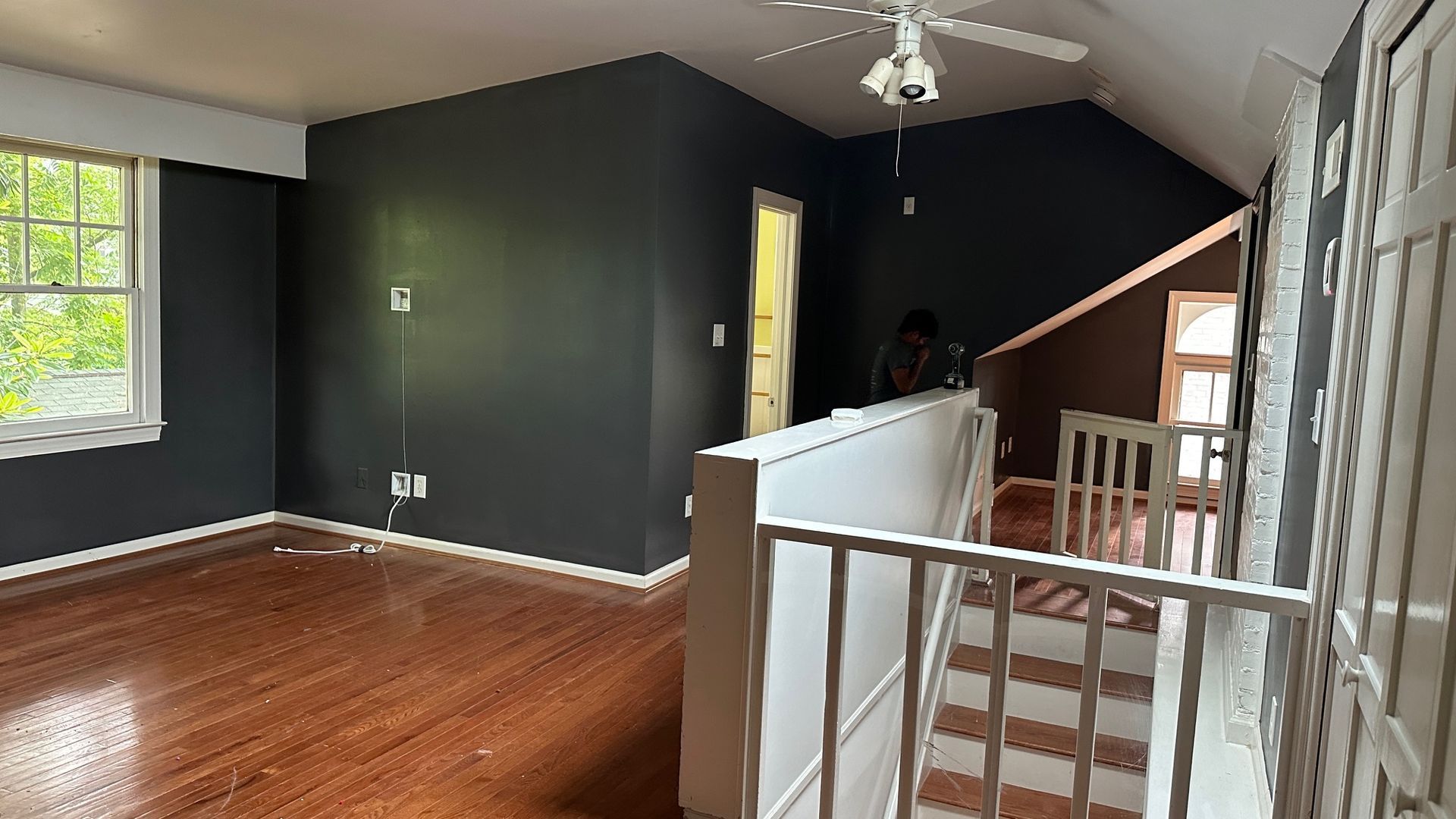 Interior view of a room with dark gray walls, wood floors, and a white ceiling fan. A staircase leads down.