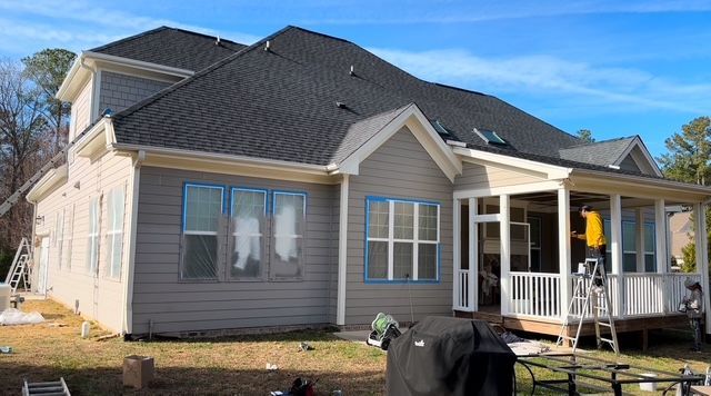 House exterior under construction, with gray siding, a screened porch, and workers on ladders.